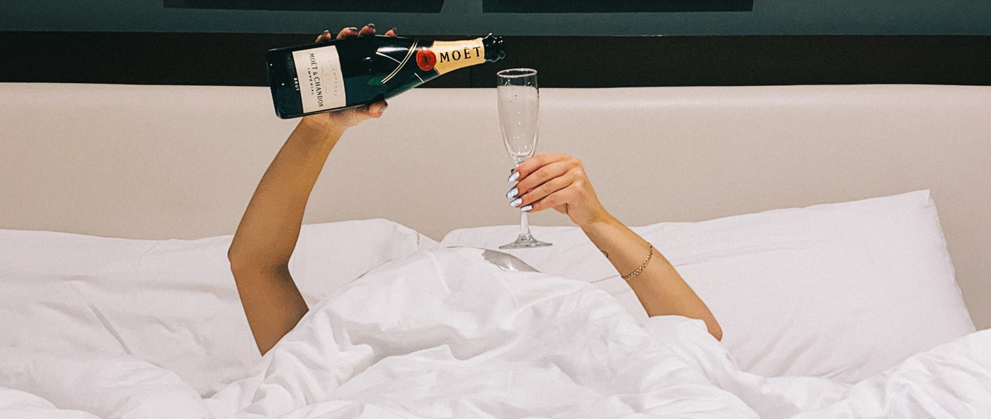 person in bed pouring themselves some wine